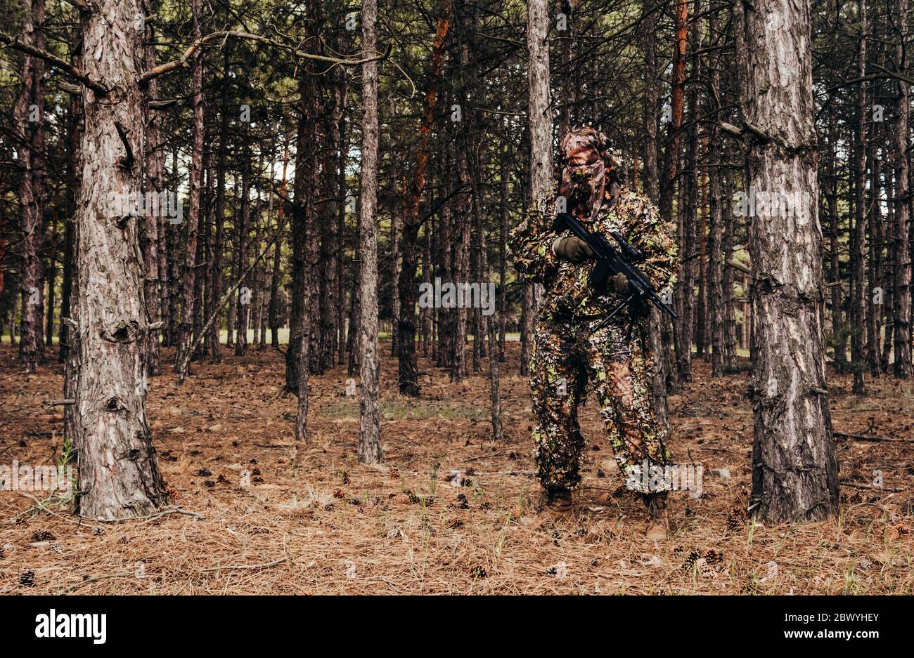 Foto di un cacciatore di cecchini mimetizzato con balestra in piedi in boschi. Foto Stock