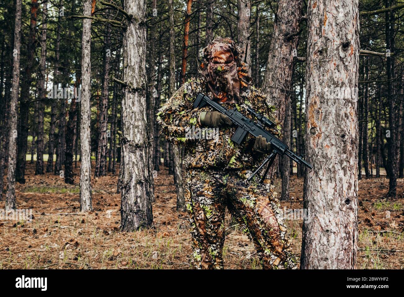 Foto di un cacciatore di cecchini mimetizzato con balestra in piedi in vista di chiocci di boschi. Foto Stock