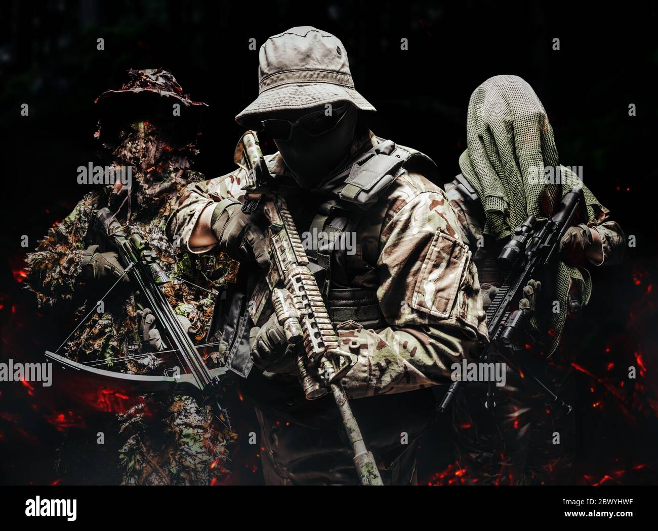 Foto di vari soldati camuffati in gilet tattico, fucili e balestra in piedi e posati su sfondo scuro con cenere fuoco. Foto Stock