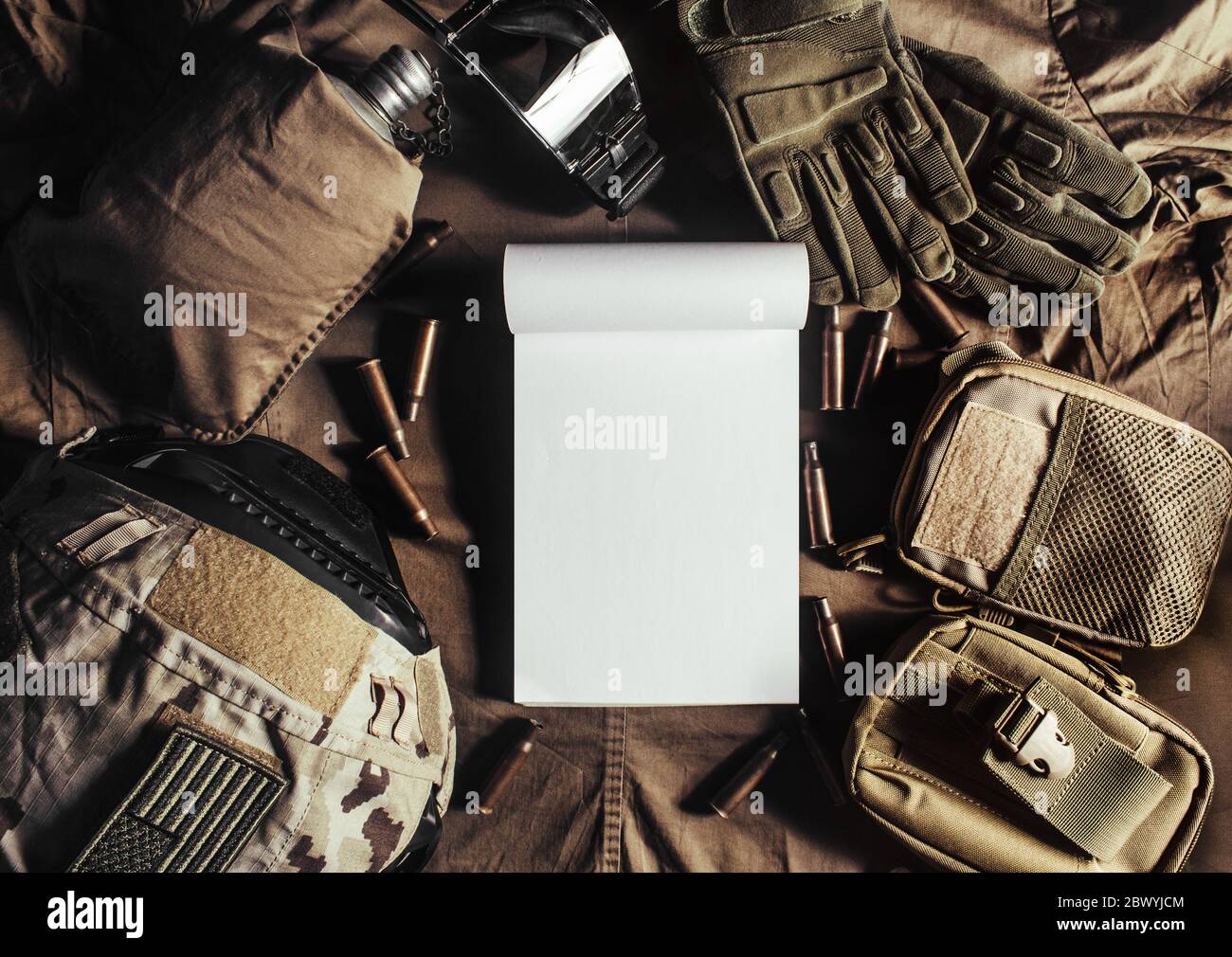 Foto di un quaderno vuoto che si stesa su un tavolo militare con casco, occhiali, proiettili, guanti e fiasca. Foto Stock