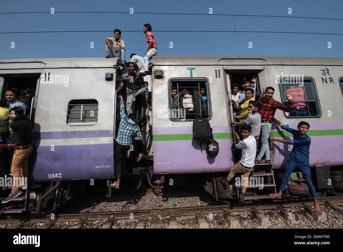 I pendolari si aggirano tra le ferrovie e si siedono sul tetto di un treno sovraffollato delle Ferrovie indiane, la stazione ferroviaria di Noli vicino a Ghaziabad, Delhi, India. Foto Stock