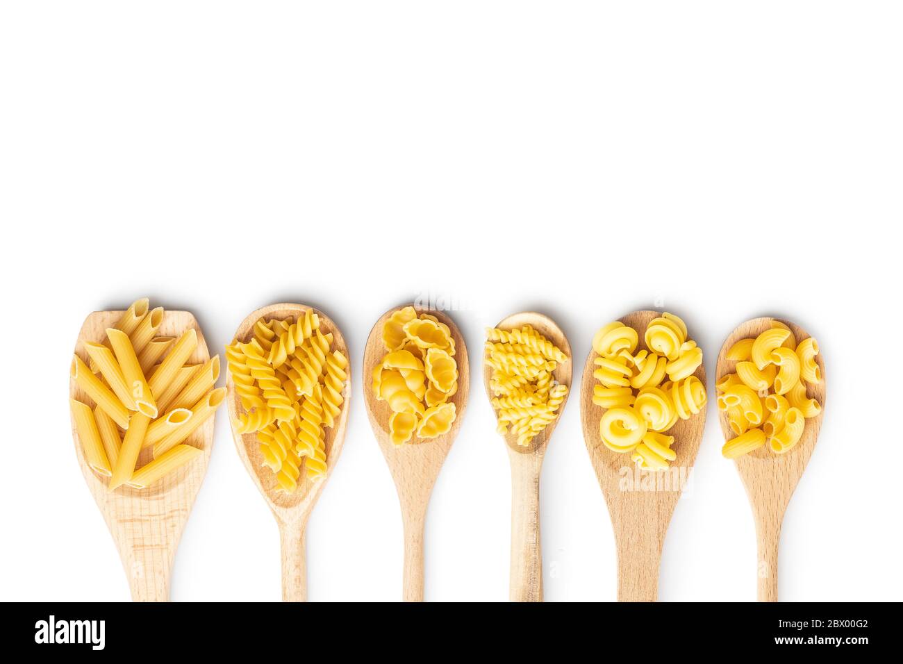 Vari tipi di pasta italiana cruda in cucchiai di legno isolati su fondo bianco. Foto Stock