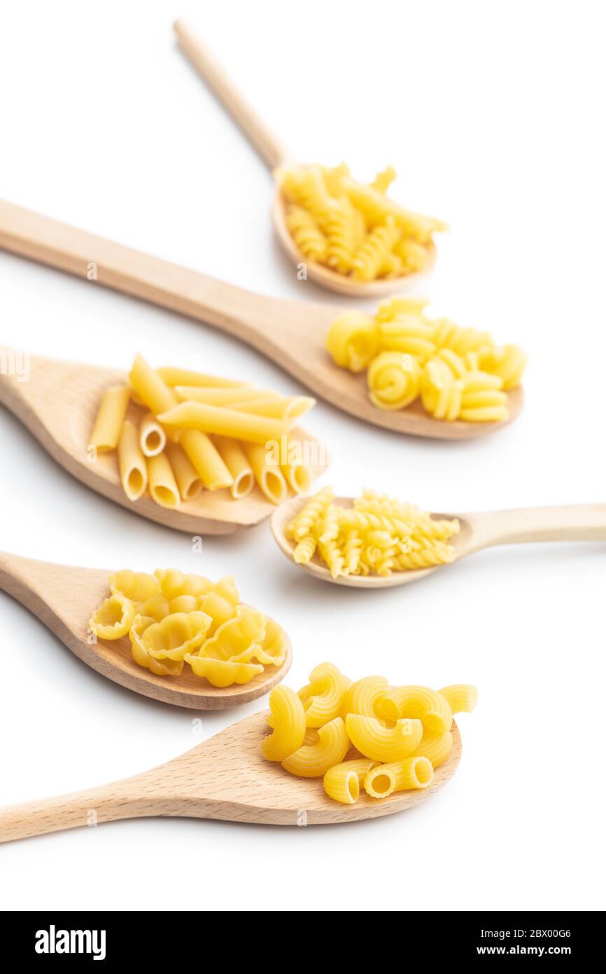 Vari tipi di pasta italiana cruda in cucchiai di legno isolati su fondo bianco. Foto Stock