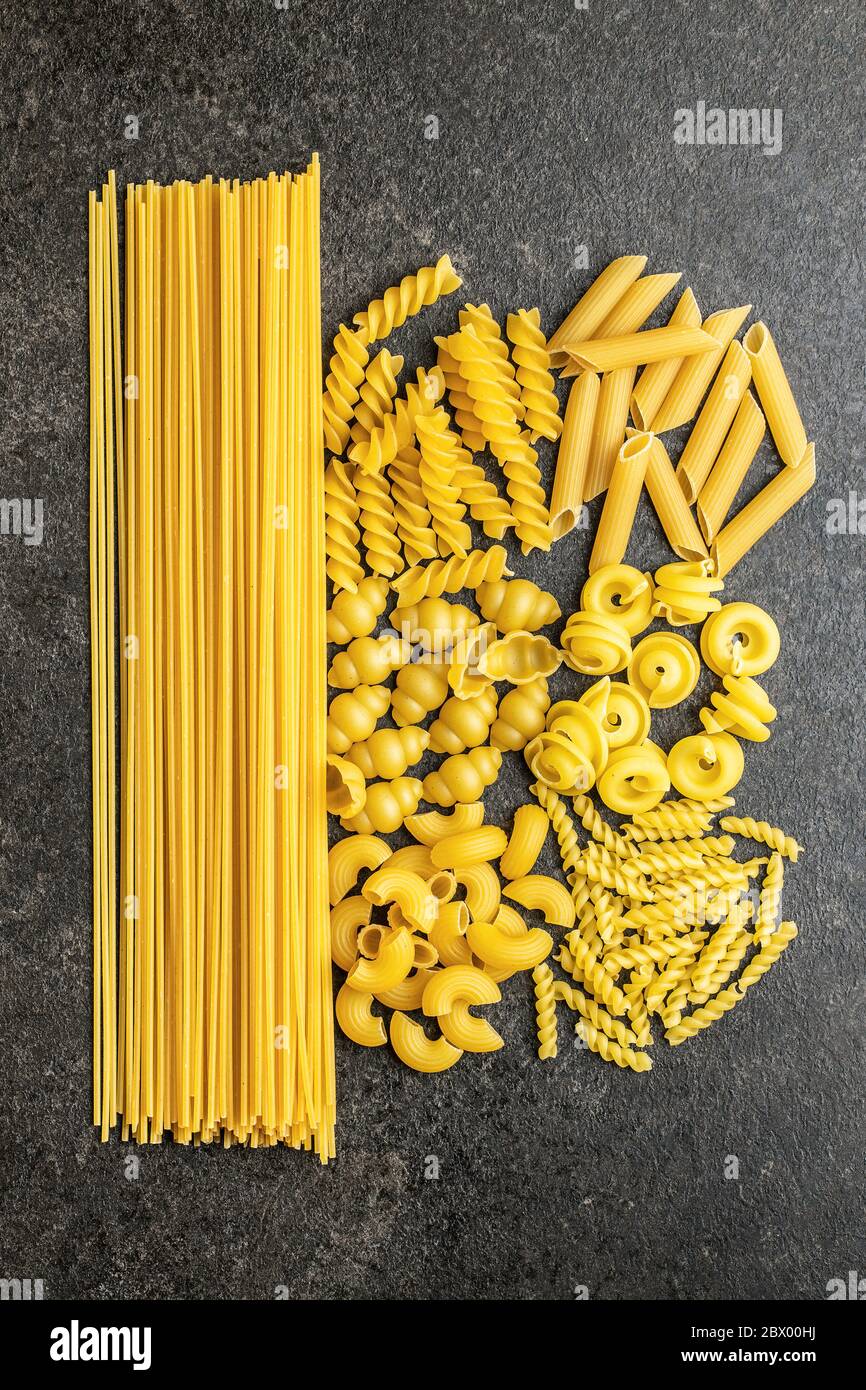 Vari tipi di pasta italiana cruda su tavola nera. Vista dall'alto. Foto Stock