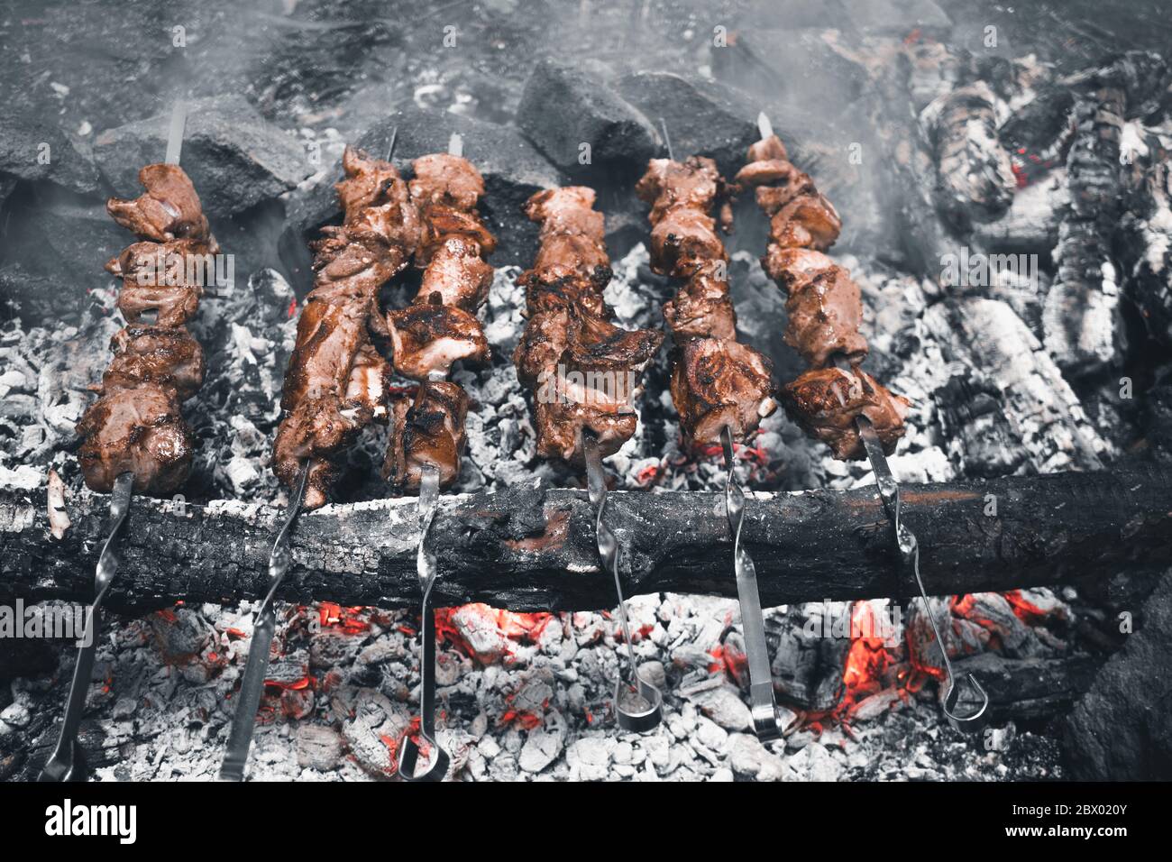 Kebab su un falò nella foresta. Gustosi e succosi pezzi di carne sugli spiedini su calici incandescenti. Natura Escursionismo Camping barbecue Foto Stock