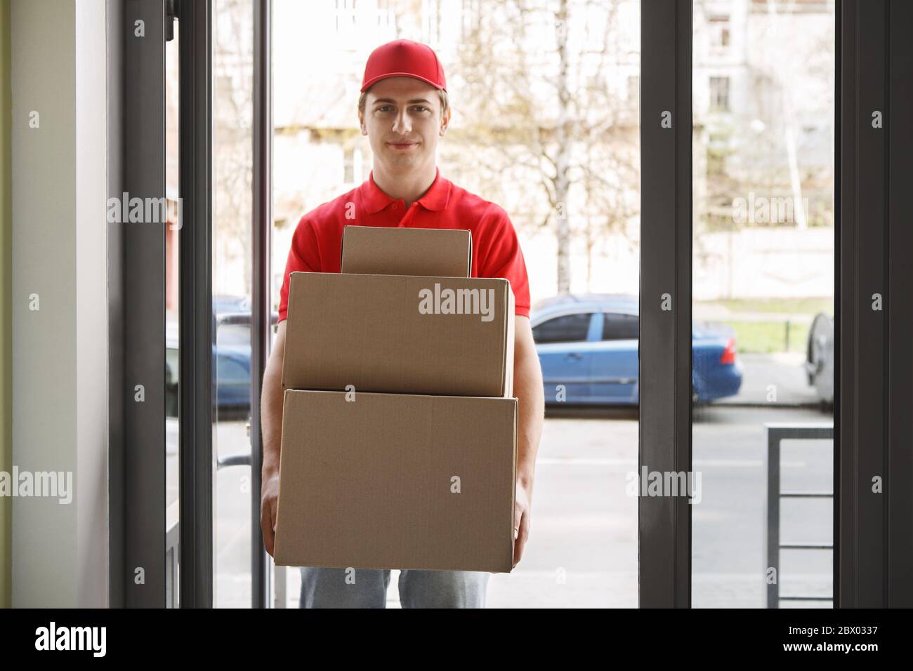 Ordini online e moderno servizio postale. Il corriere in uniforme rossa contiene molte scatole Foto Stock