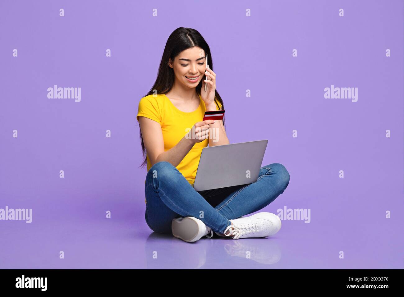 Ragazza asiatica che parla sul cellulare, facendo ordine con il portatile e la carta di credito Foto Stock