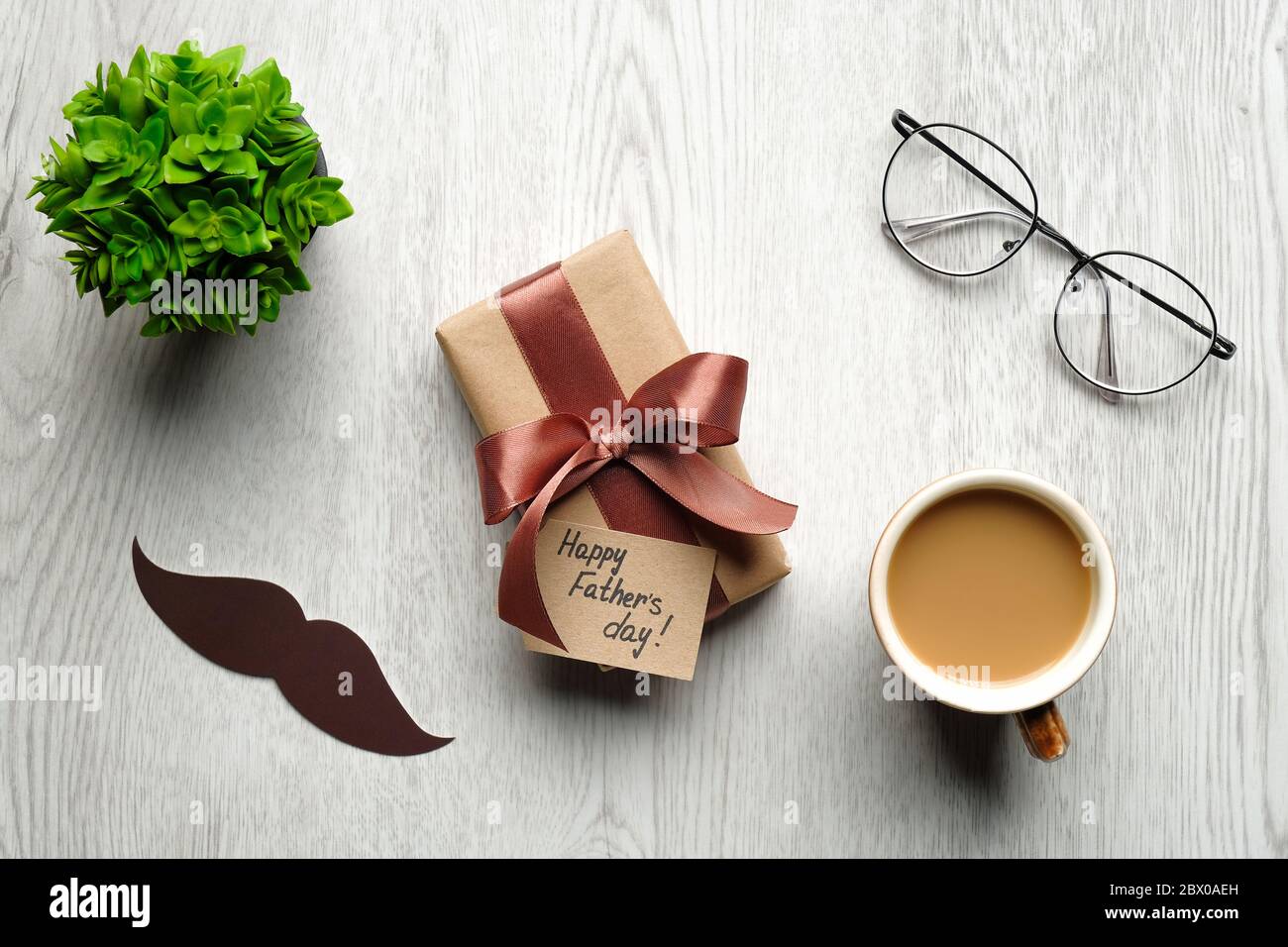 Concetto di Giornata del Padre felice. Composizione piatta con confezione regalo o regalo per papà, baffi, tazza da caffè, bicchieri, fiore su tavolo di legno. Vista dall'alto. Foto Stock
