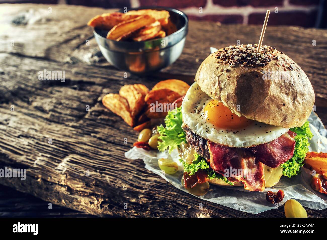Hamburger di manzo con uova fritte, pancetta, lattuga, spicchi di patate e uva su un legno rustico Foto Stock