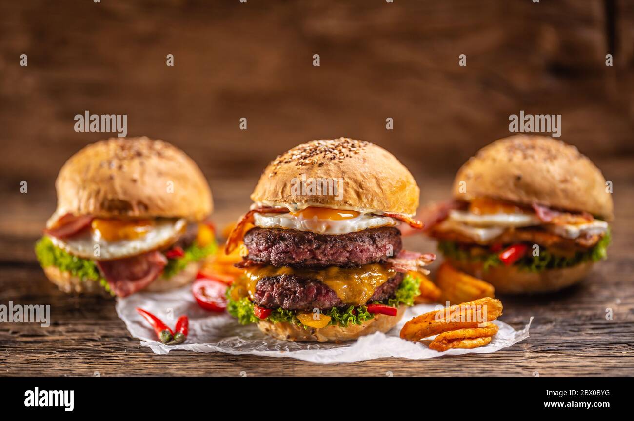 Menu di hamburger gustosi e succosi con hamburger di manzo doppio sul davanti con spicchi di patate e peperoncino e altri due hamburger sul retro Foto Stock