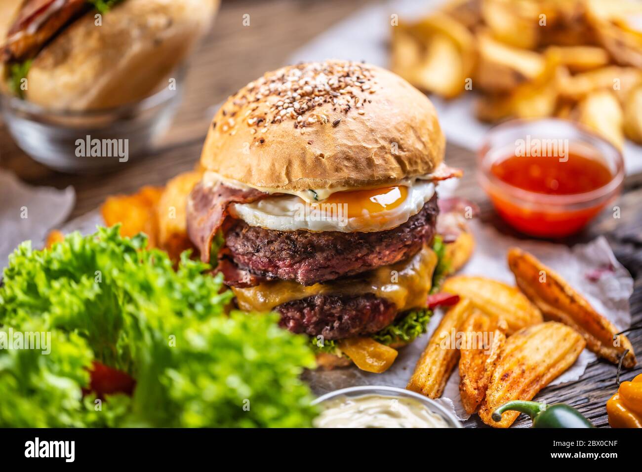 Hamburger doppio di manzo con pancetta e formaggio e lattuga, patatine e salsa su un lato Foto Stock