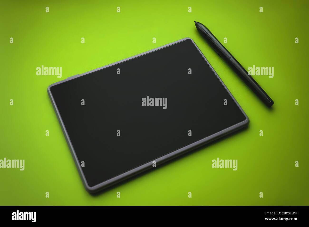 Penna grafica per tablet sulla superficie del dispositivo, foto in primo piano. Tavoletta grafica con penna per illustratori e designer, su sfondo verde Foto Stock