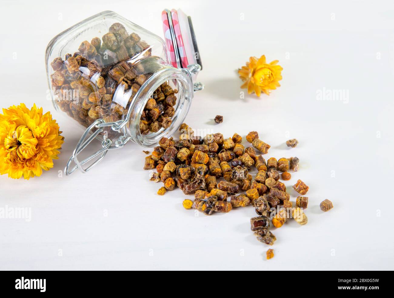 Medicina alternativa, pane di api fatto di miele domestico (fiore fermentato e polline di pianta) all'interno di un piccolo vaso di vetro e sparso su tavola bianca. Foto Stock