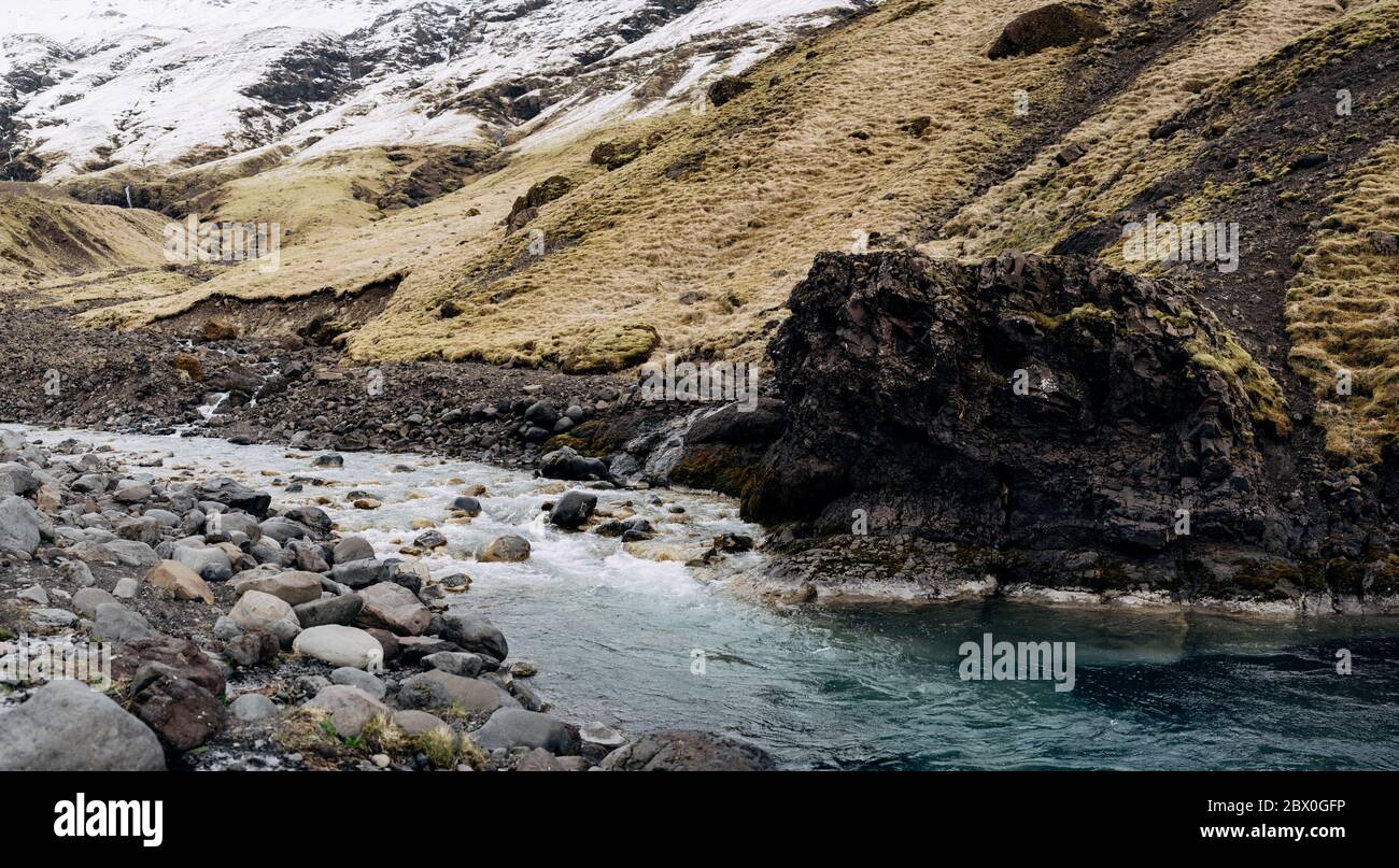 Un fiume di montagna poco profondo con acqua azzurra scorre sullo sfondo delle montagne nelle cime mth e innevate. Foto Stock