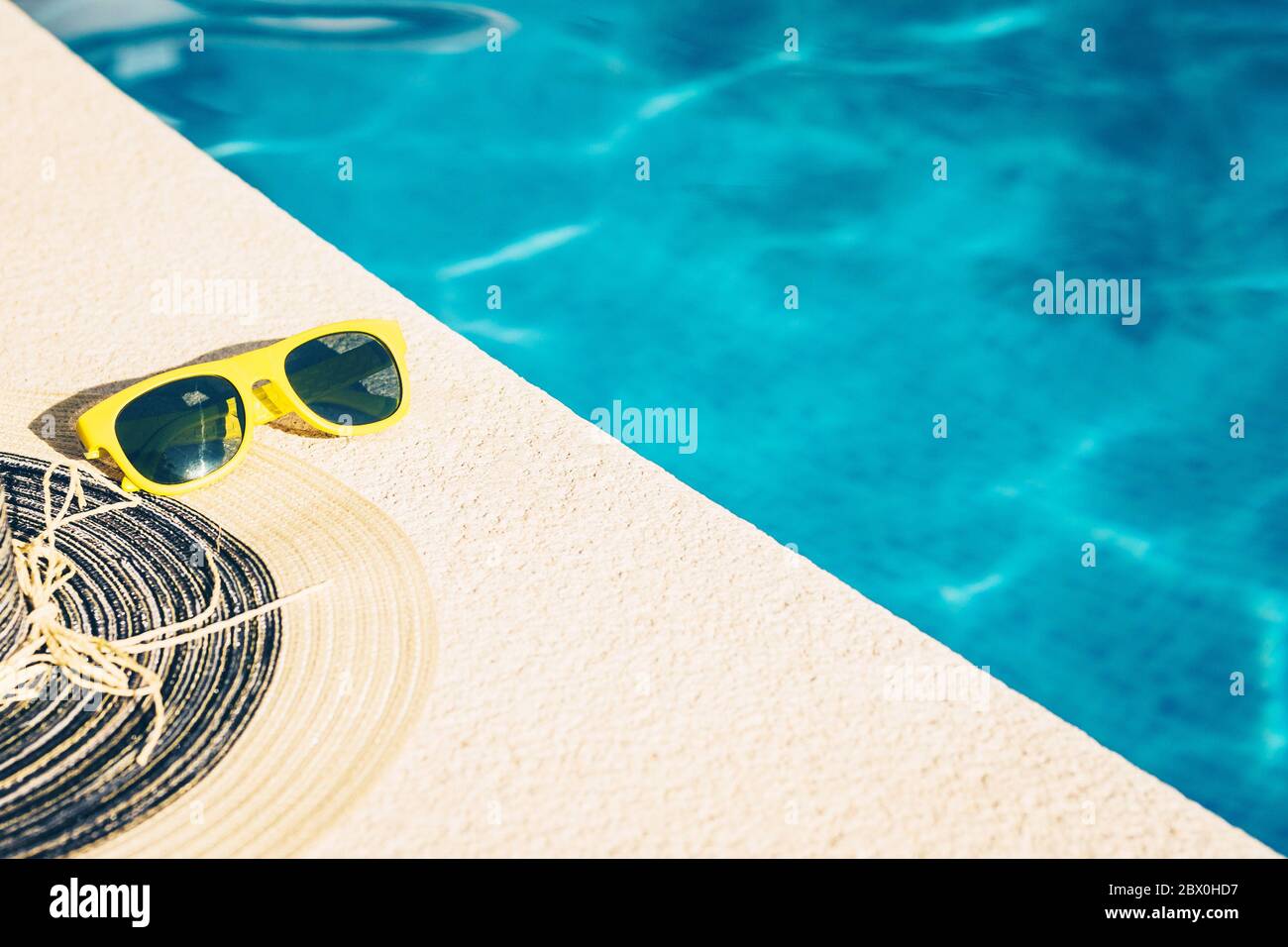 Occhiali da sole di plastica gialli e un cappello di paglia su una pietra vicino all'acqua sono blu luminoso - una calda giornata estiva Foto Stock