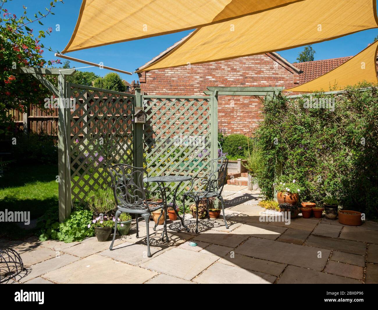 Piccolo patio giardino con ombrellone giallo, triangolare e cielo blu sopra in una soleggiata giornata estiva, Inghilterra, Regno Unito Foto Stock