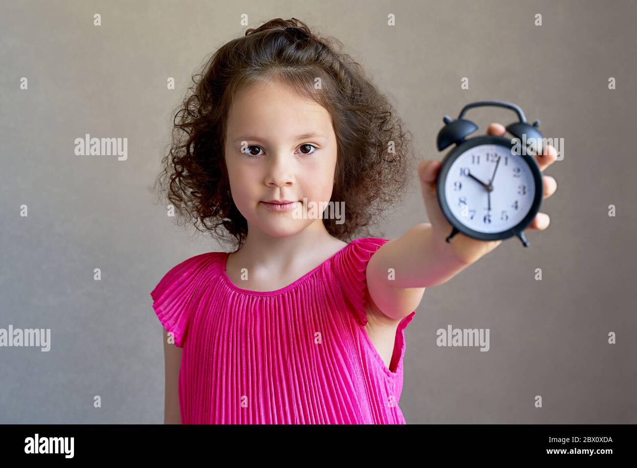 Bella bambina riccia con un orologio da scrivania Foto Stock