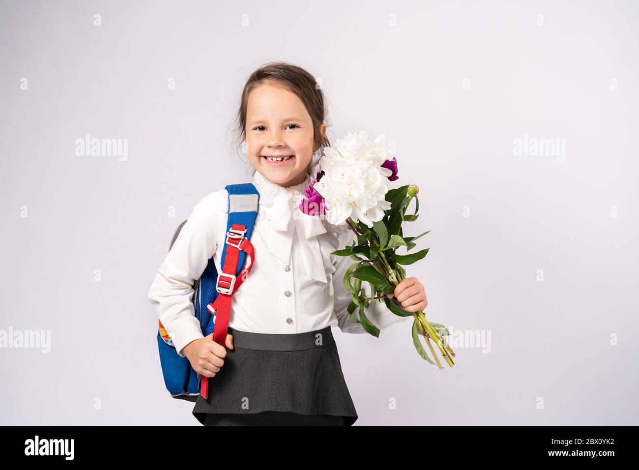 ragazza di scuola di primo grado in una camicia bianca che tiene i fiori e uno zaino Foto Stock