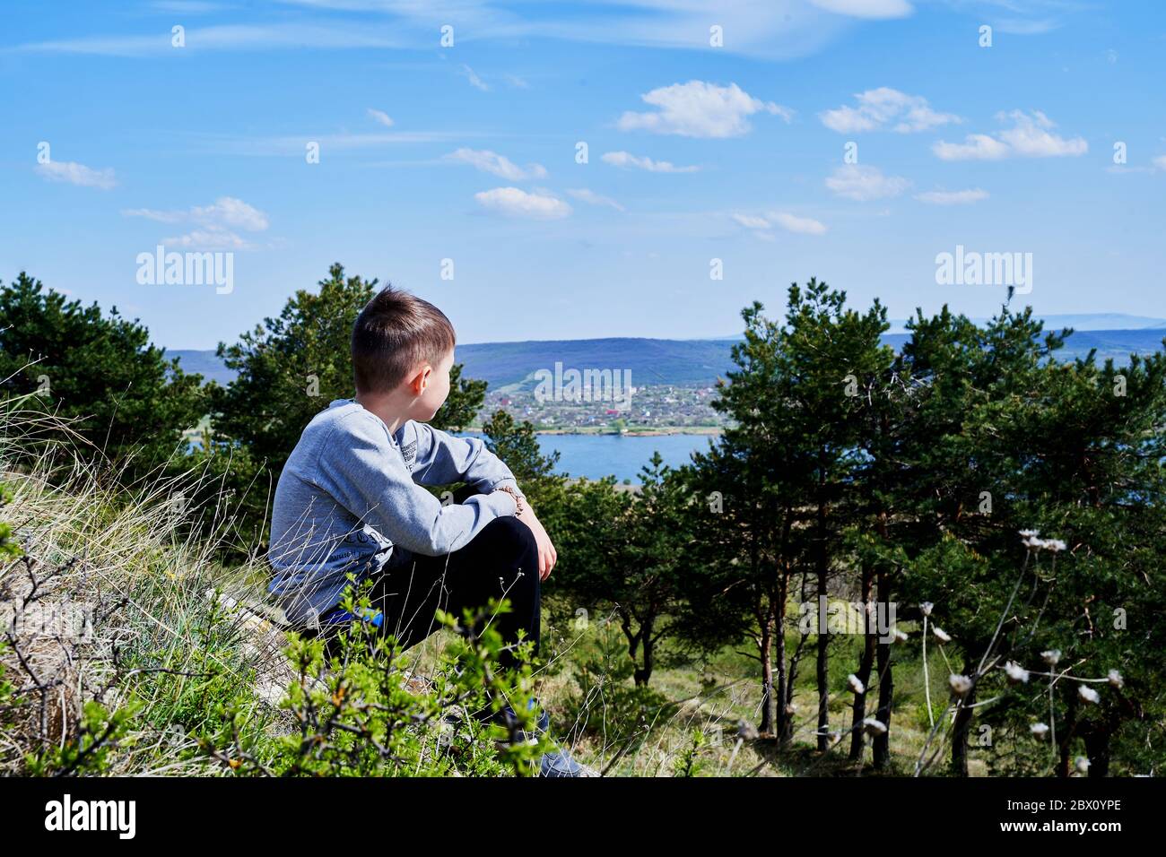 un ragazzo si siede su una collina e guarda lago Foto Stock