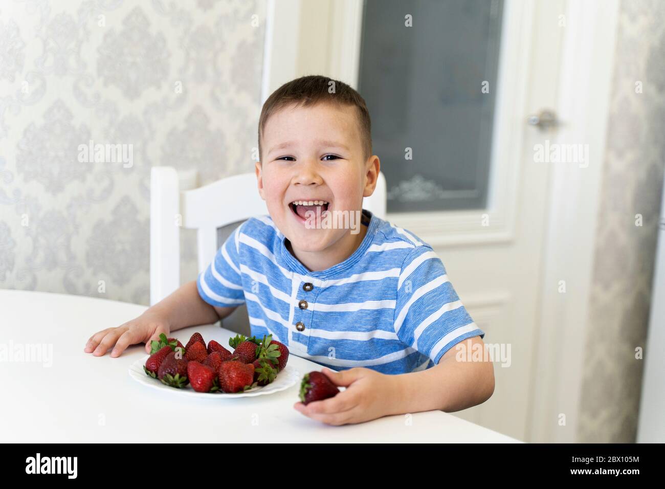 bambino divertente ride e mangia fragole. primavera. Aprile-maggio. Foto Stock