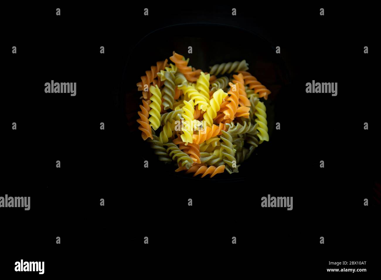 Composizione di fusilli tricolori crudi, a forma di torcente. Primo piano e fuoco selettivo sulla pasta colorata di fusilli, isolata su nero Foto Stock