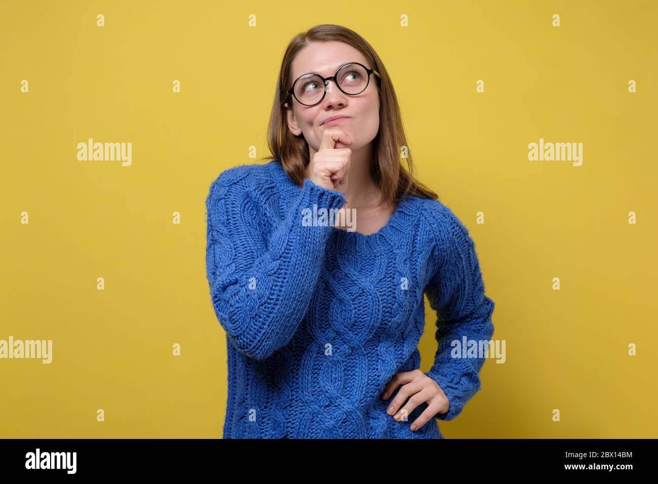 Pensare donna in blu maglione meditare su qualcosa di importante. Studio girato su parete gialla. Foto Stock
