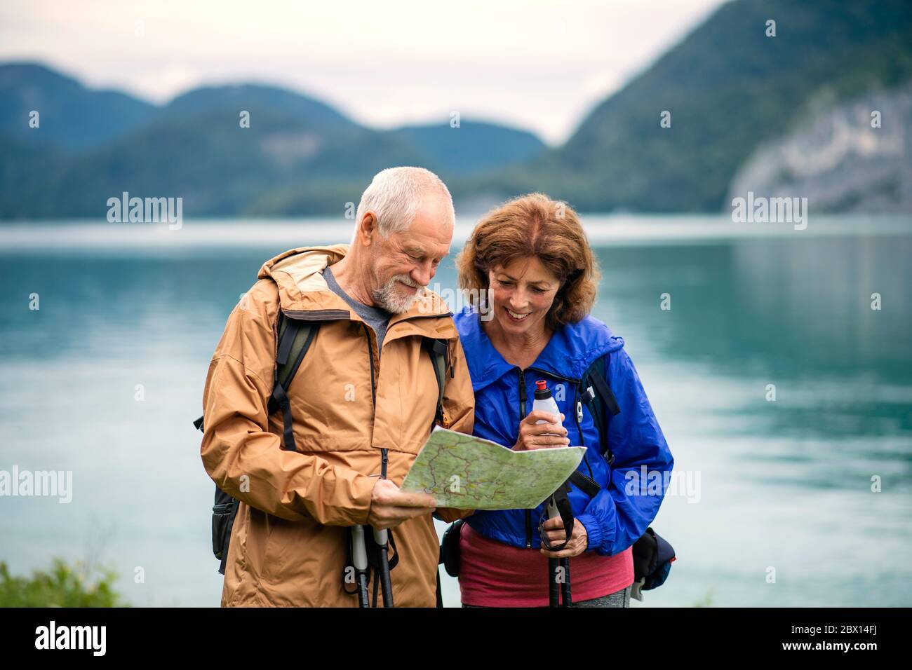 Una coppia di anziani pensionati escursionisti in piedi vicino al lago in natura, utilizzando la mappa. Foto Stock