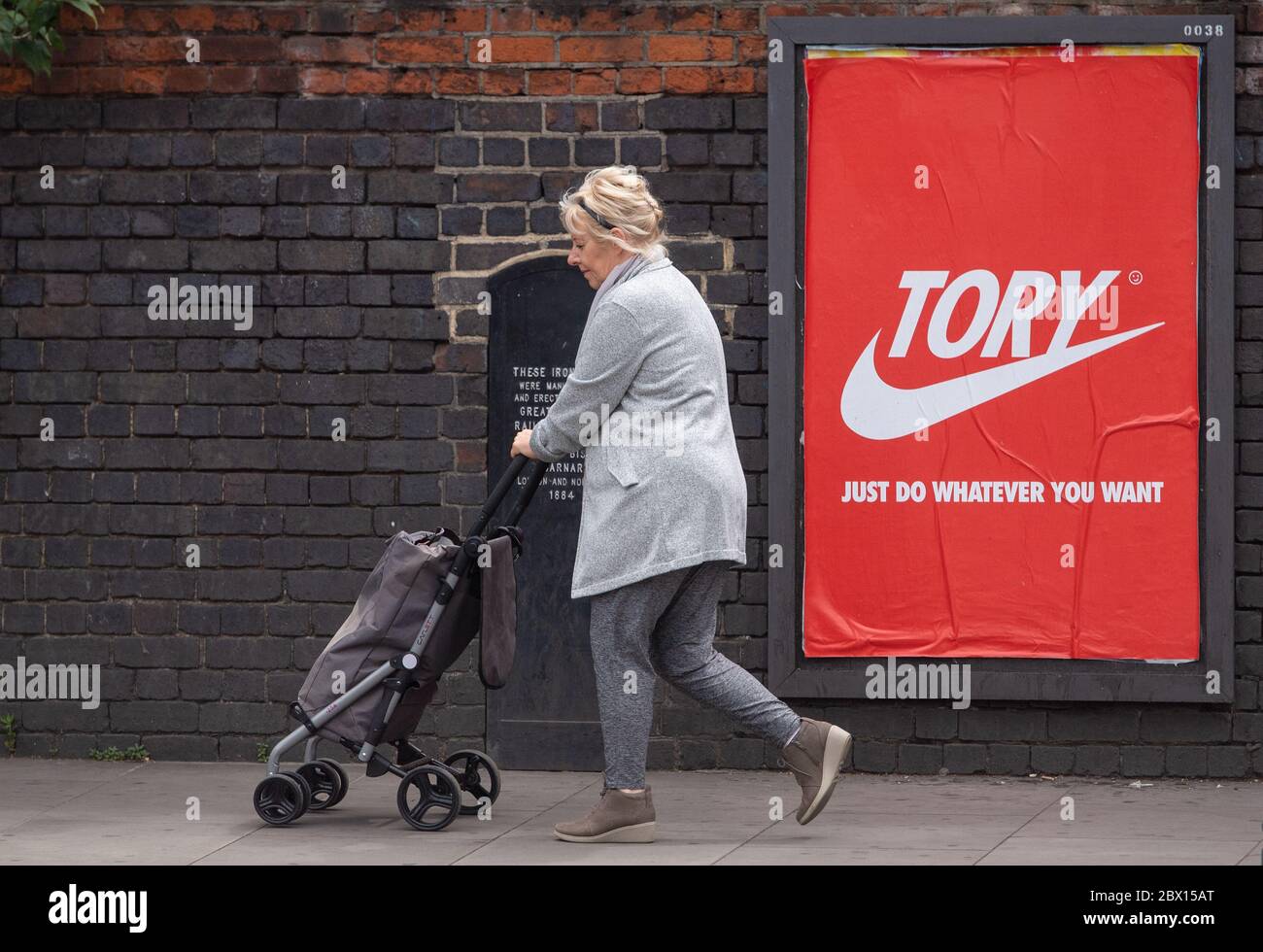 Una donna passa un poster che legge 'Tory - Just Do Anywhat you want', a Shoreditch, a est di Londra, dopo l'introduzione di misure per portare l'Inghilterra fuori dal blocco. Foto Stock