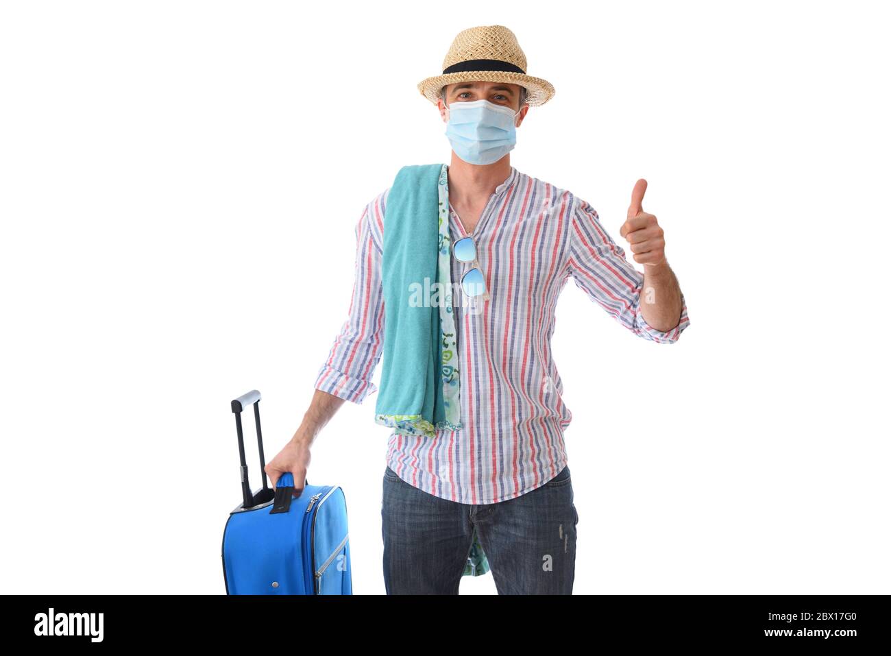 Felice uomo pronto a viaggiare in vacanza durante la stagione del coronavirus con i pollici su vestito ok per l'occasione con accessori da spiaggia e valigia è Foto Stock