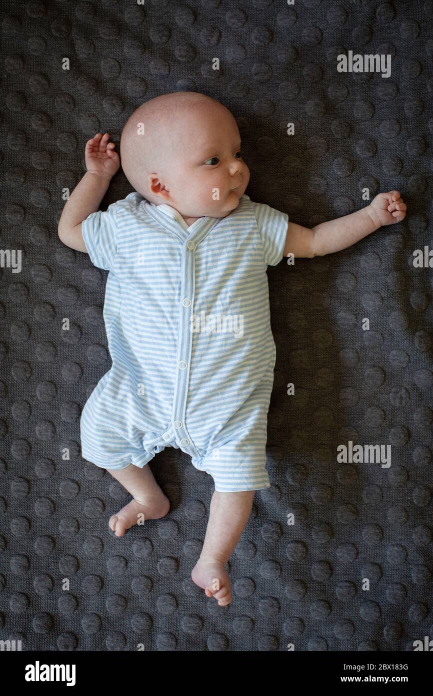 Un bambino neonato che si stesa su un tappeto scuro. Foto di Sam Mellish Foto Stock