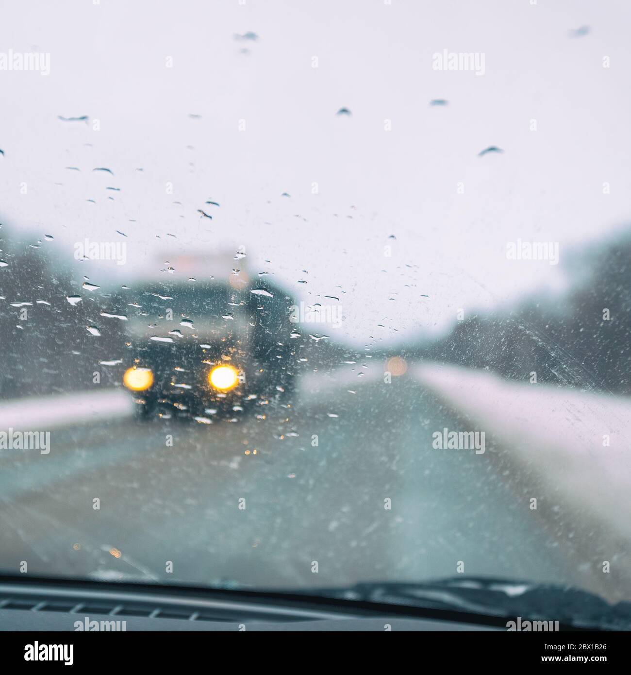 Vista offuscata attraverso il parabrezza nelle gocce di pioggia sull'autostrada, che si sta muovendo verso una grande auto. Messa a fuoco selettiva Foto Stock