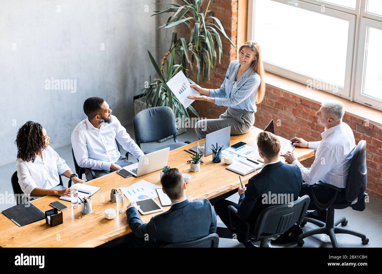 Donna d'affari che mostra grafici ai colleghi che analizzano l'efficacia aziendale in ufficio Foto Stock