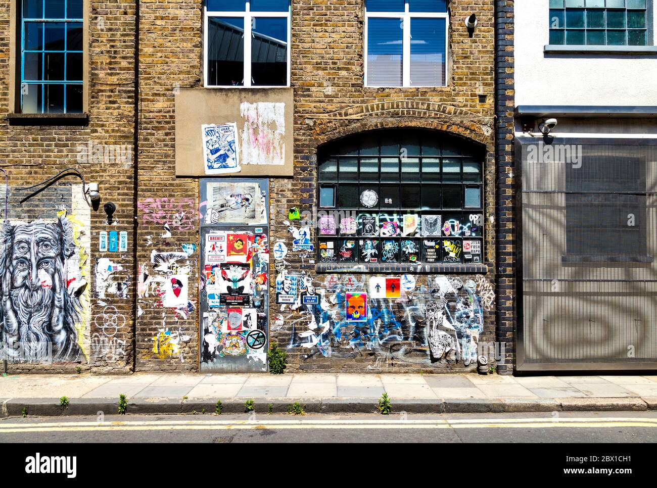 Muro in mattoni coperto di graffiti, etichette e poster in Fashion Street, Spitalfields, Londra, Regno Unito Foto Stock