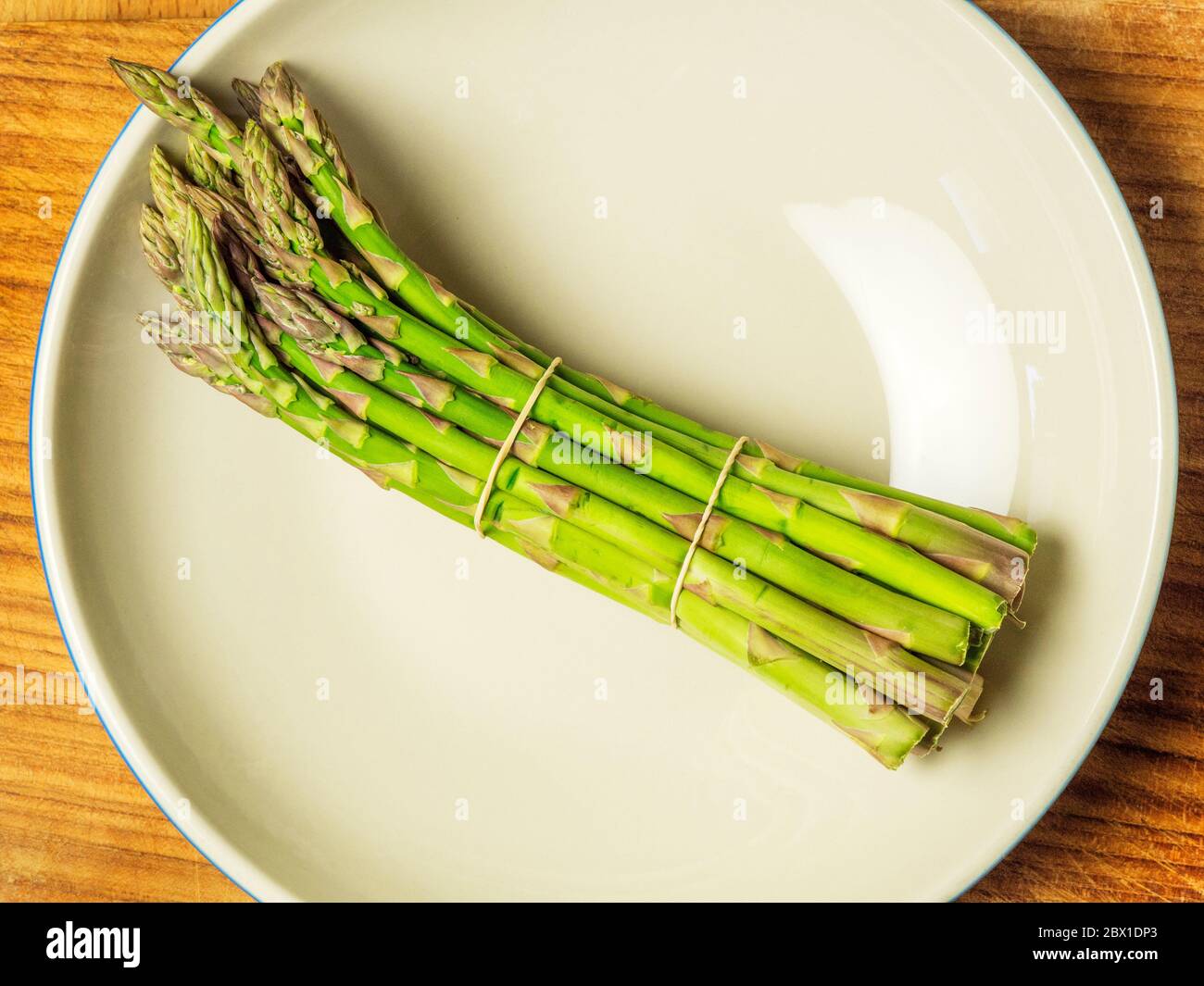 Un mazzo di asparagi in una ciotola su un tagliere di legno Foto Stock