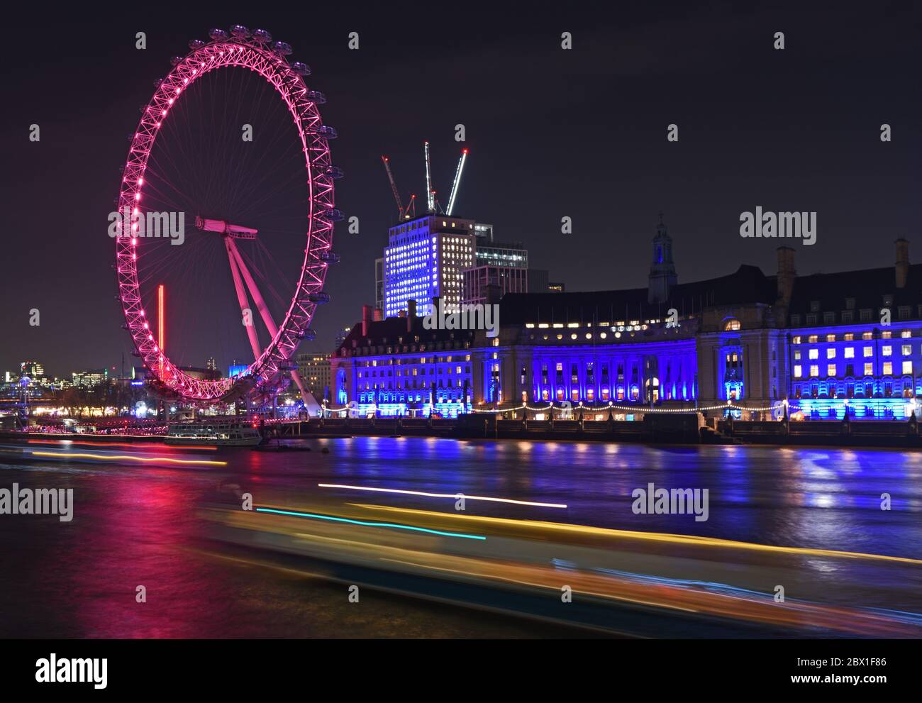 Vista notturna del London Eye sulla riva sud del Tamigi. Include sentieri leggeri dal traffico fluviale in primo piano. 11 dicembre 2018 Foto Stock