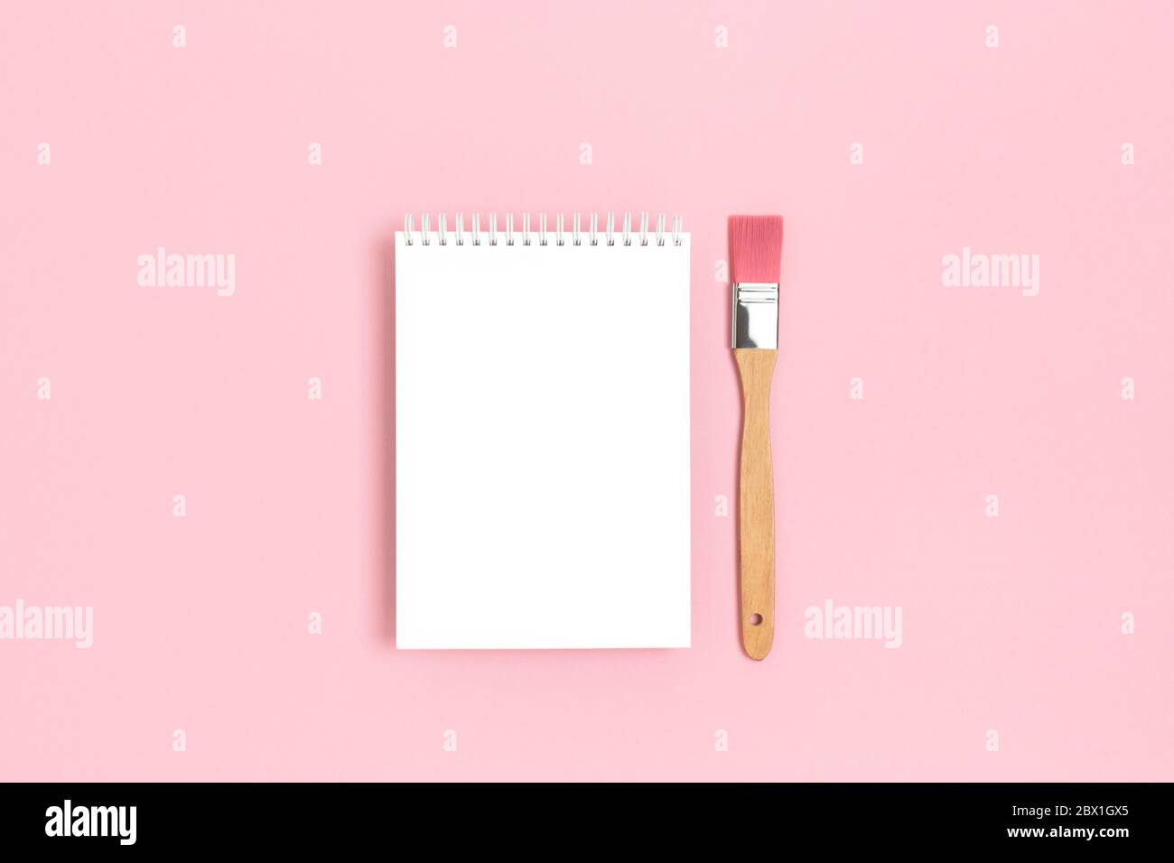 Modello vuoto per notebook con pennello su sfondo rosa pastello. Mockup artistico. Foto Stock