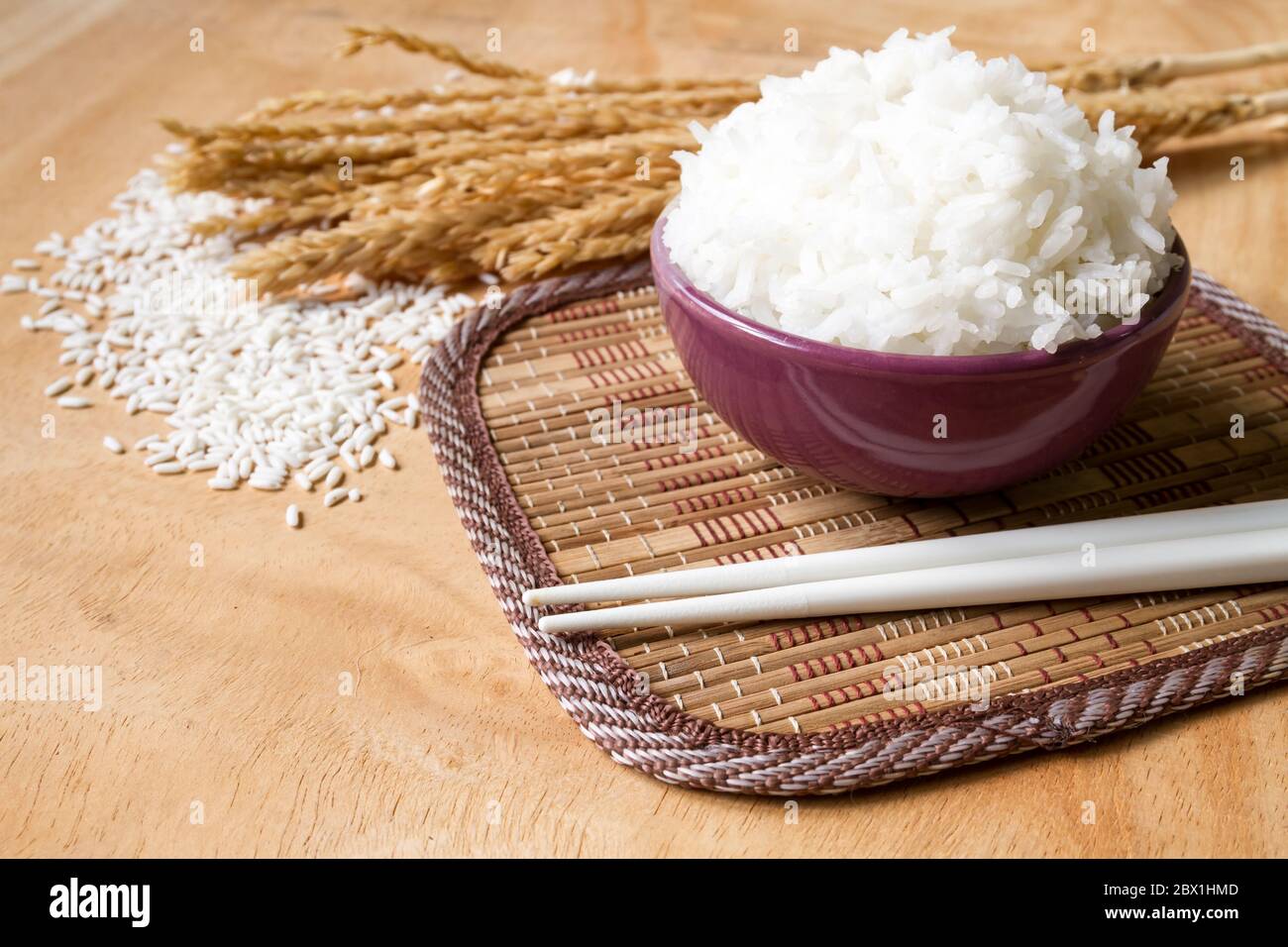 Riso cotto in ciotola con grano di riso grezzo e pianta di riso secco su  sfondo di tavola di legno Foto stock - Alamy