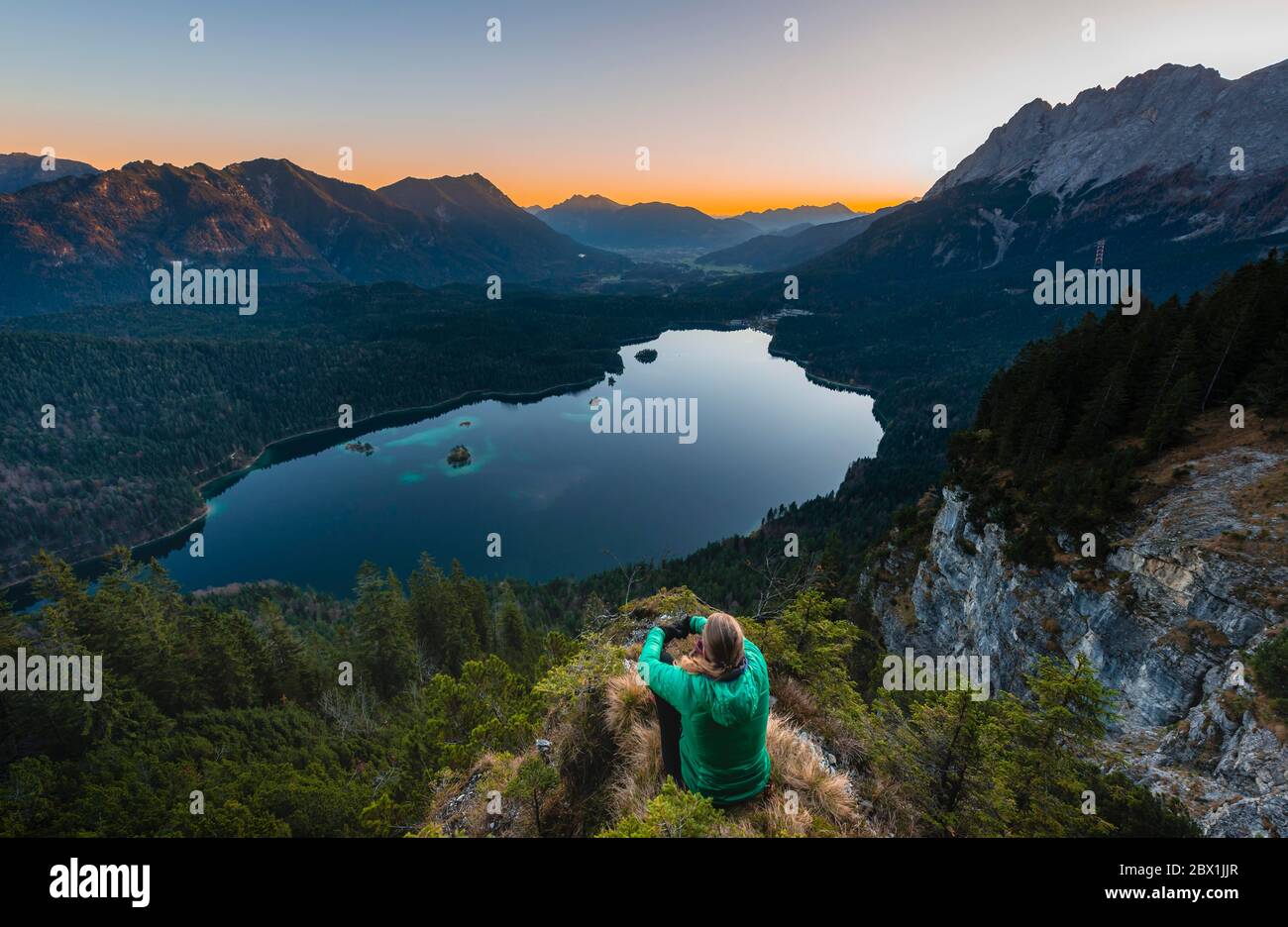 Donna che guarda sul lago Eibsee e sul massiccio di Zugspitze con Zugspitze, alba, catena montuosa di Wetterstein, vicino a Grainau, alta Baviera, Baviera, Germania Foto Stock