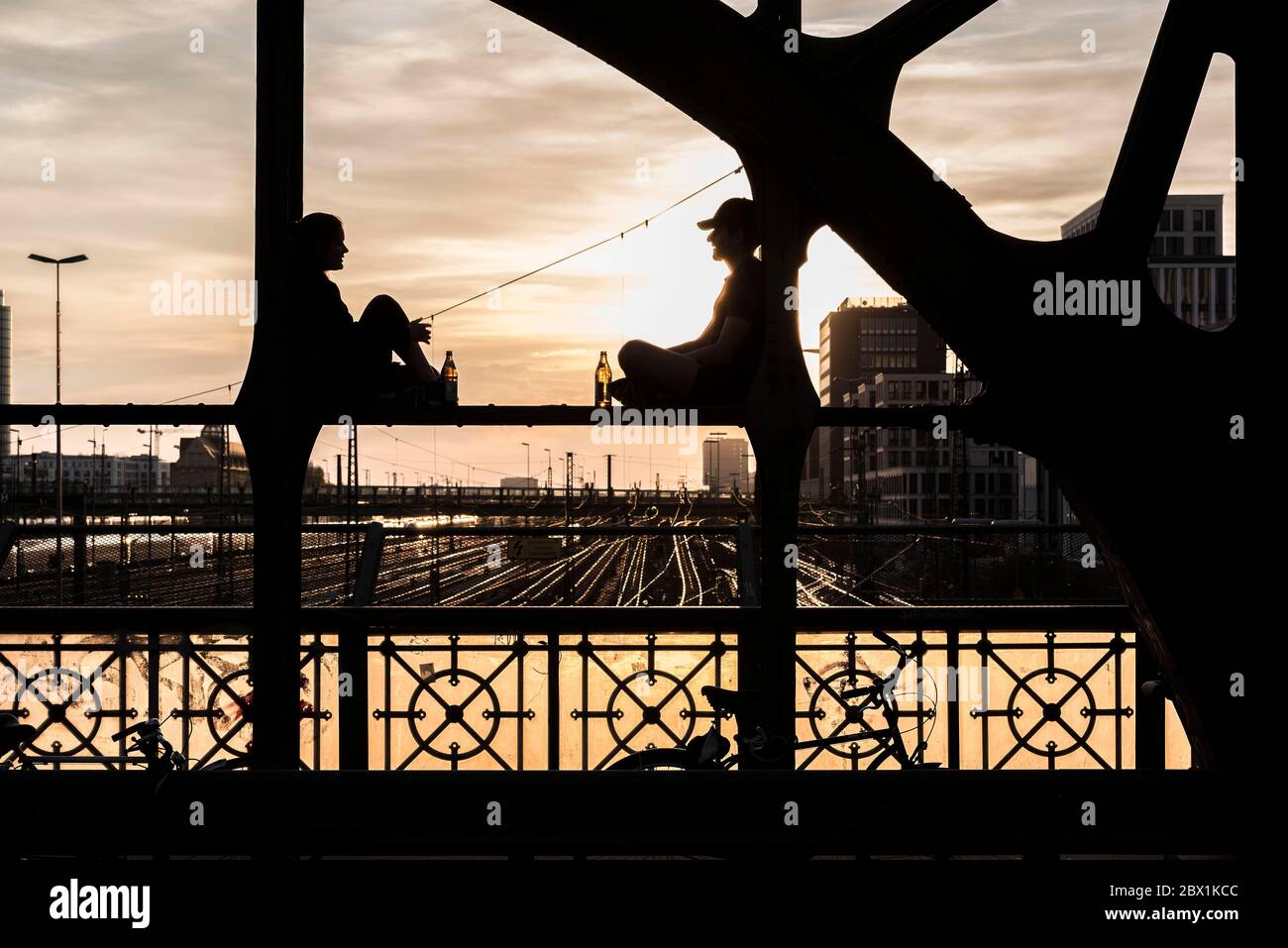 Due persone sedute sul parapetto e bevute contro la luce, Haccurbruecke, Monaco, Baviera, alta Baviera, Germania Foto Stock