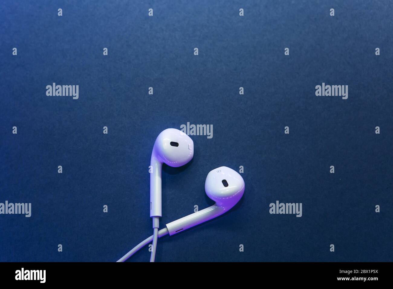 Cuffie bianche cablate su sfondo blu in stile minimalista. Foto Stock