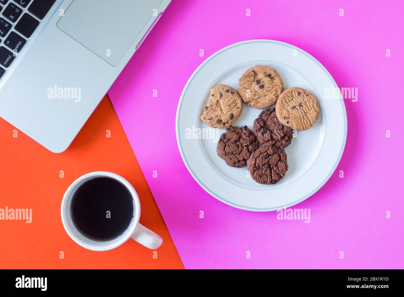 Biscotti con caffè e computer portatile su sfondo colorato. Foto Stock