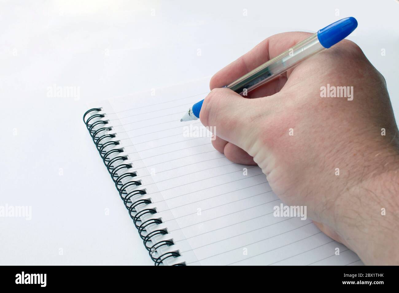Mano maschile primo piano con una penna a sfera su un blocco note su sfondo bianco Foto Stock