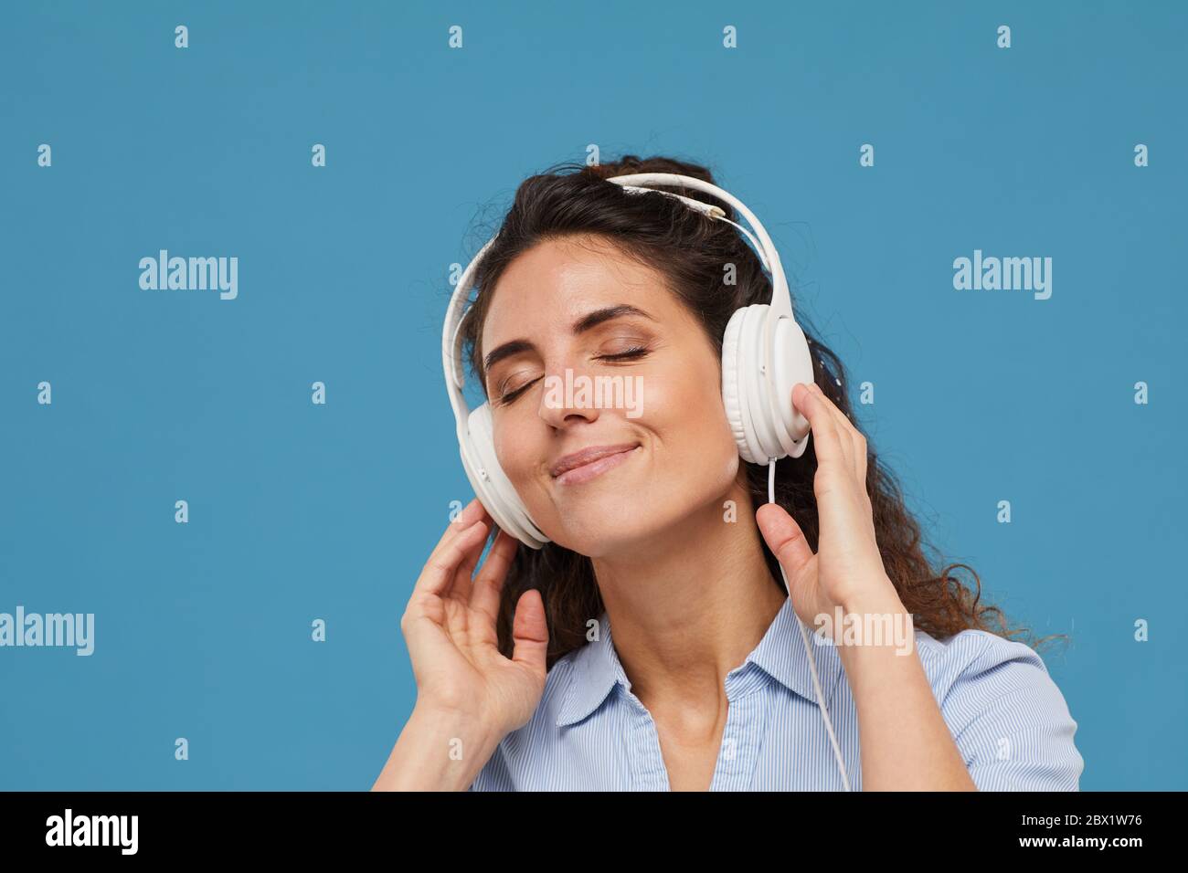 Giovane donna in cuffia che ascolta la musica su sfondo blu Foto Stock
