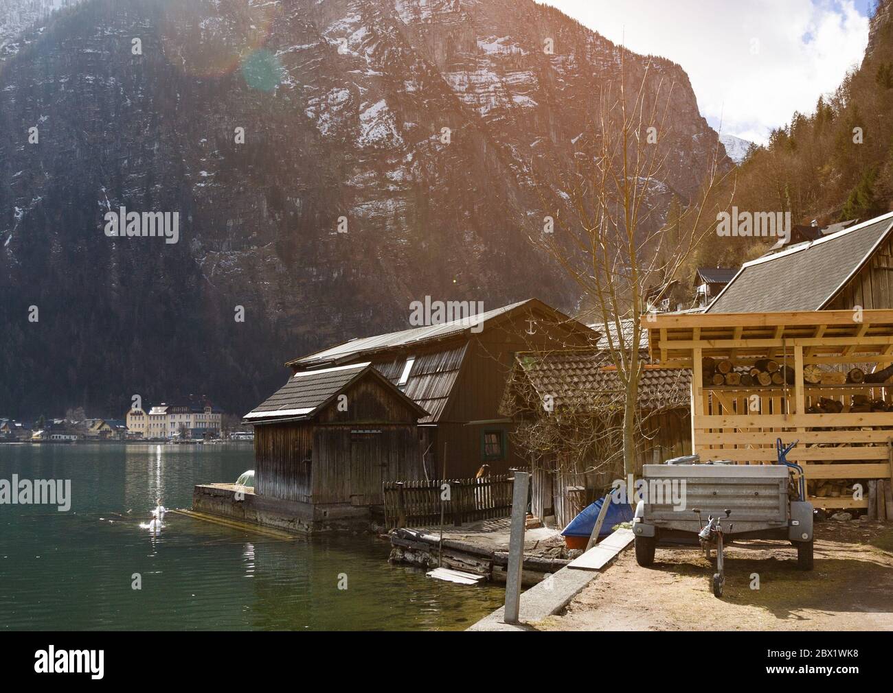 Lago Halstatter in raggi di sole vicino a tradizionali case in legno e contro le montagne nel villaggio di Hallstatt, Salzkammergut Foto Stock