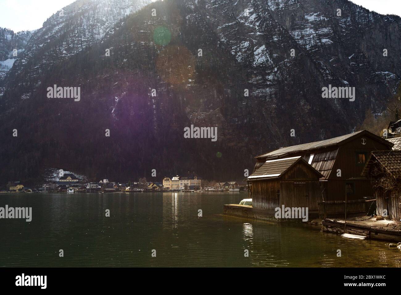 Lago Halstatter in raggi di sole vicino a tradizionali case in legno e contro le montagne nel villaggio di Hallstatt, Salzkammergut Foto Stock