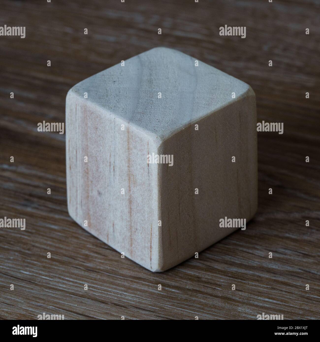 Un blocco o cubo di legno liscio che mostra tre lati vuoti su uno sfondo di legno con contrasto elevato e spazio di copia Foto Stock