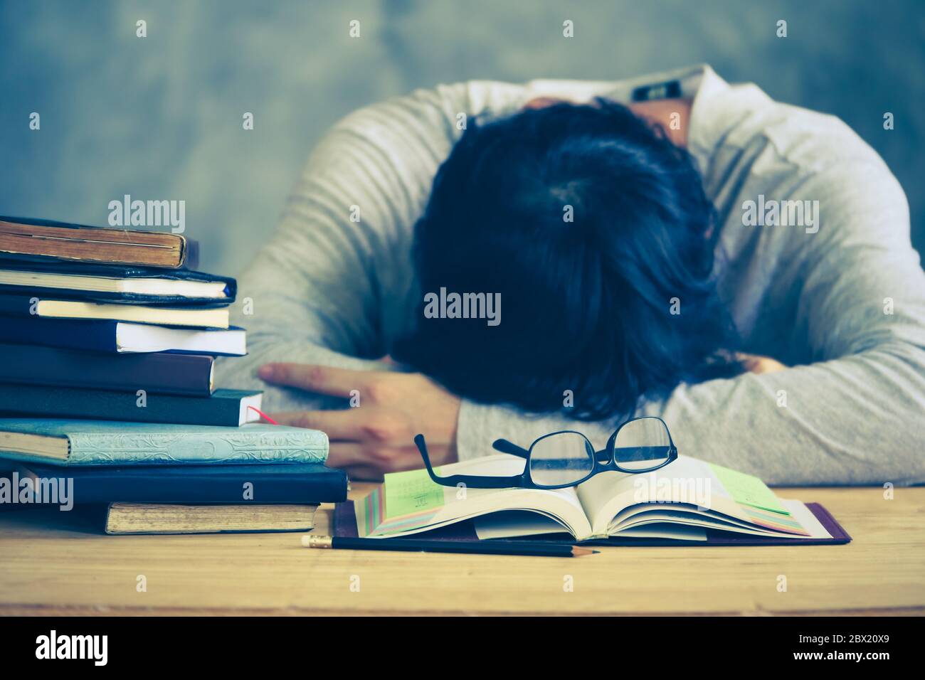 Stanco giovane uomo che dorme con le pile di libri sul tavolo di legno. Tonalità vintage Foto Stock