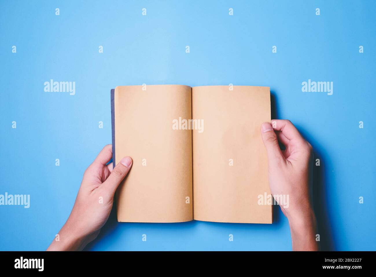 Vista dall'alto delle mani che tengono un libro vuoto pronto con spazio per la copia pronto per il testo su sfondo blu. Foto Stock