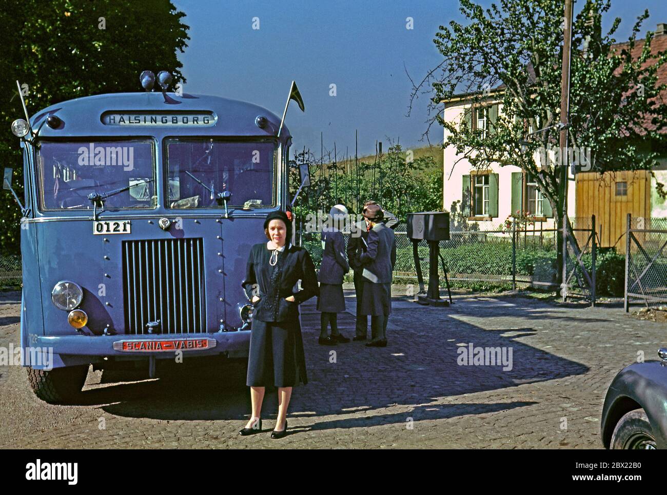 Una donna si trova accanto a un autobus, che è diretto per Helsingborg, Svezia c. 1950. Indossa abiti alla moda. Altri passeggeri aspettano in background. L'autobus è uno Scania Vabis (parte successiva di Saab-Scania). Ha due bandiere svedesi o pennant attaccati alla parte anteriore. Helsingborg (Hälsingborg, 1912-1970) è una città di Scania, Svezia, ed è il punto più vicino della Svezia alla Danimarca. Foto Stock