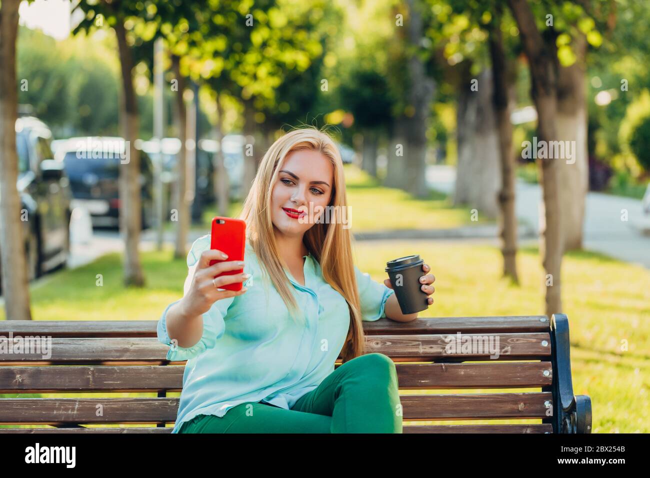 felice sorriso bella blusa blu donna elegante seduta su una panca e prendendo selfie sul telefono Foto Stock